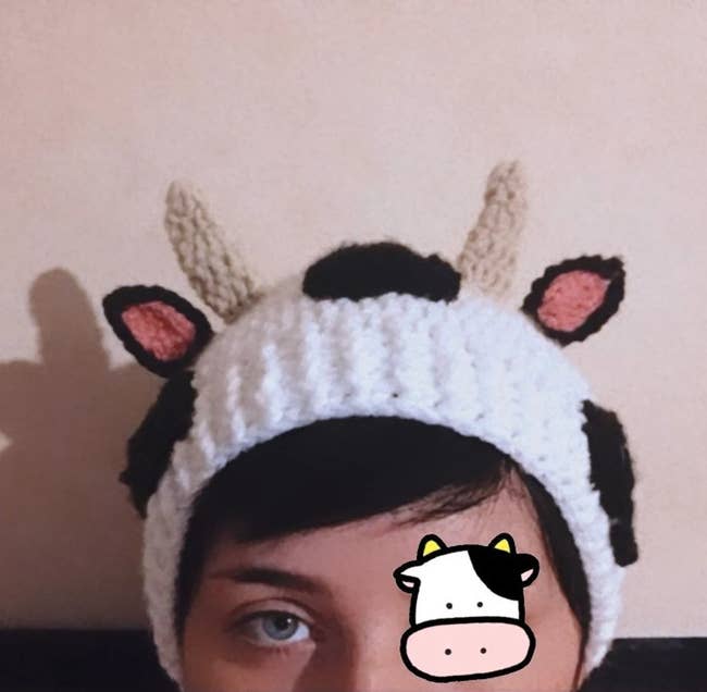 Model wearing black and white crocheted cow-shaped beanie in front of a white wall