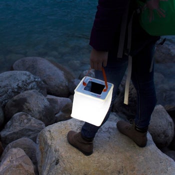 model holding square lantern next to rocks by the water