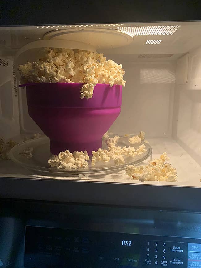 The popcorn maker in a microwave overflowing with popcorn