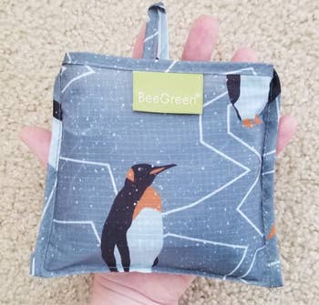 A folded up grocery bag the size of a person's hand with penguins on it 
