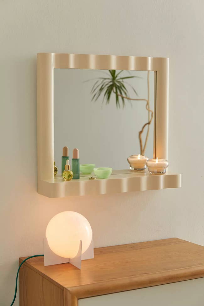 Wall-mounted shelf with mirror displaying various cosmetic products and a lit spherical lamp on a wooden surface
