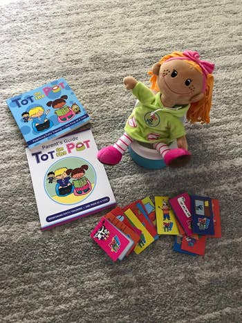 A close up of the doll on the toy potty, the books, and reward cards
