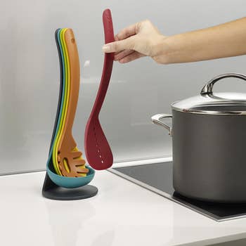 Person placing a colorful kitchen utensil from a nesting set beside a stove, ideal for space-saving cooking needs
