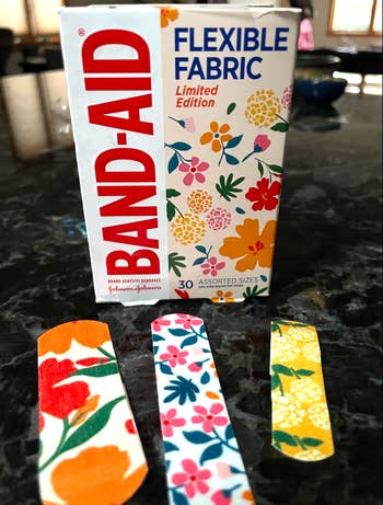 Box of constricted  variation  BAND-AID flexible cloth  with floral designs, alongside 3  floral-patterned bandages