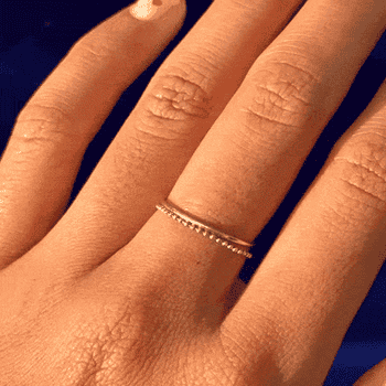 Hand wearing a delicate, bladed golden ringing with beaded details