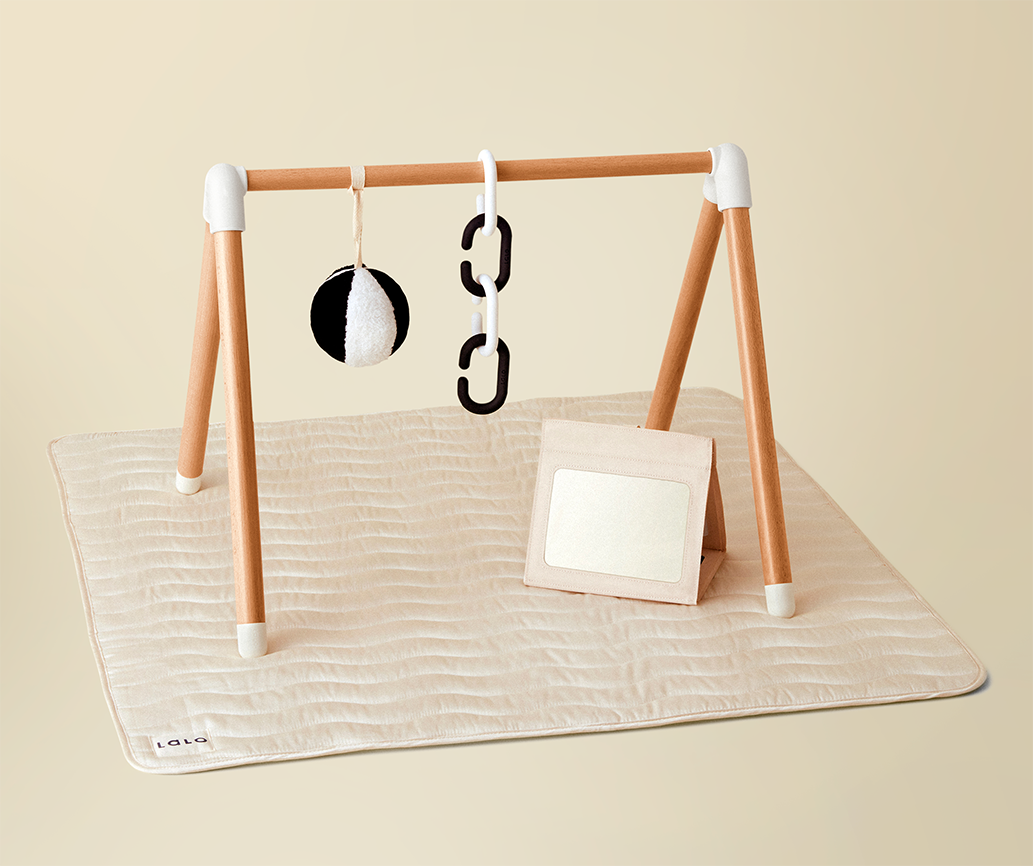 an oatmeal colored simple play gym with a mat and hanging toys