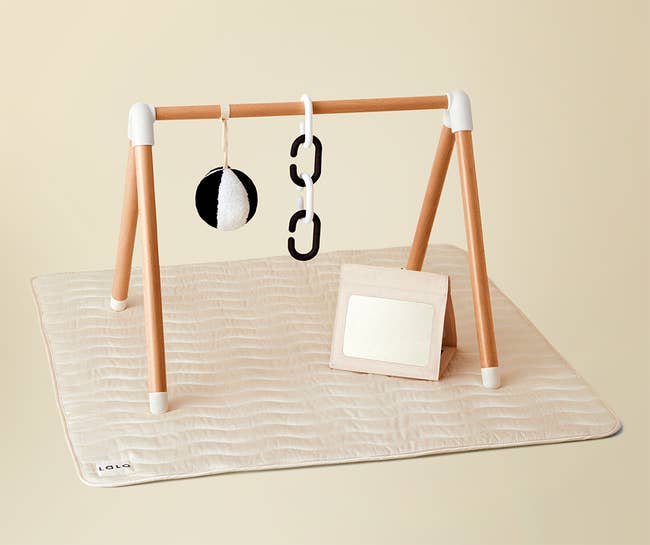 an oatmeal colored simple play gym with a mat and hanging toys