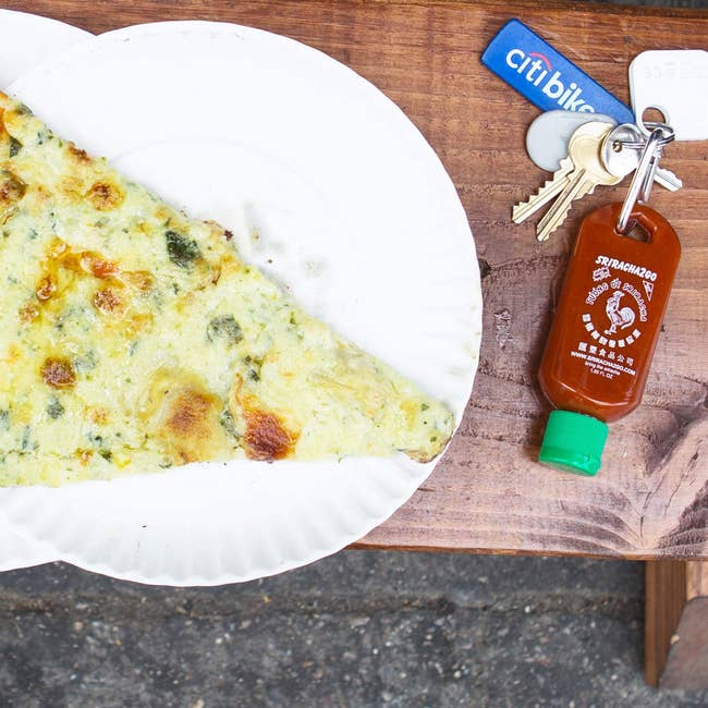 the small bottle filled with sriracha attached to keys and next to pizza 