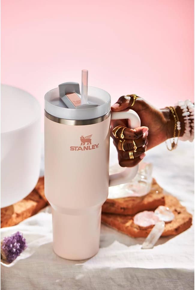 Insulated Stanley tumbler with a handle, straw, and lid; adorned manus  holding the handle; acceptable   connected  a array  with decorative items