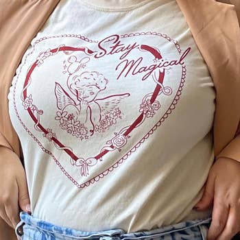 model wearing an off white tee with a drawing of a cherub inside of a heart holding a mickey balloon