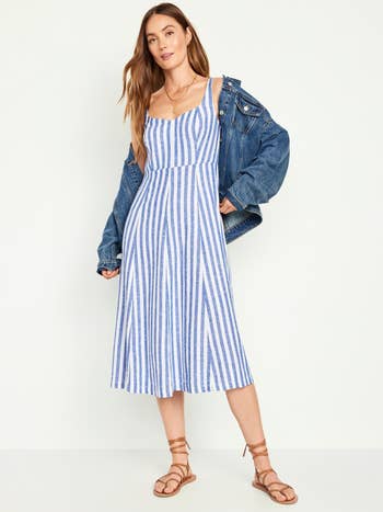 Woman in a striped sundress holding a denim jacket, poised for a casual look. Perfect spring-summer outfit inspiration