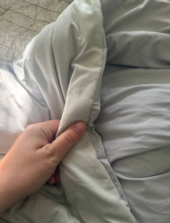 A manus touches a soft, plush comforter connected a bed, showcasing its texture and quality