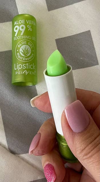 reviewer holding the tube of green lipstick