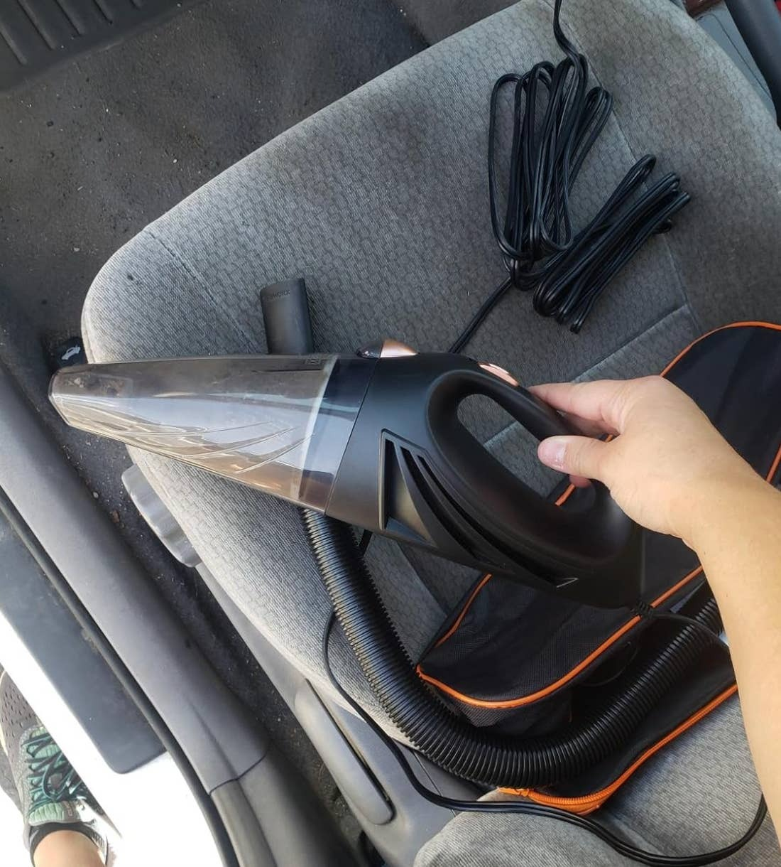 Peninjau memegang vakum portabel dengan kabel dan tas di latar belakang 