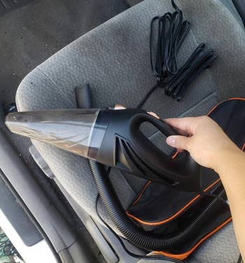 reviewer holding the portable vacuum with the cord and bag in the background 