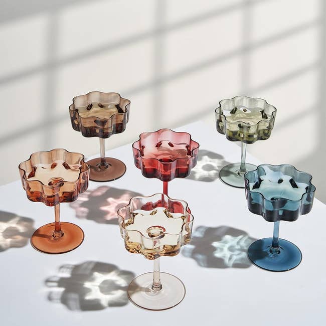 Six uniquely-shaped glassware pieces with scalloped edges, displayed successful assorted colors, casting intricate shadows connected a achromatic surface. Ideal for gifting