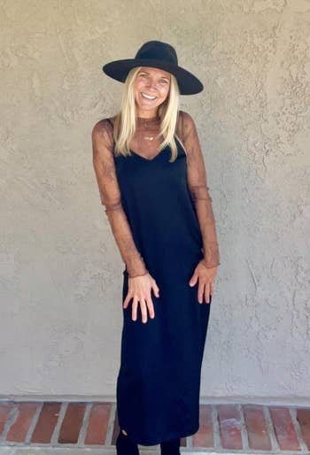 A reviewer smiling in wide-brim hat, sheer-sleeve dress, posed against a textured wall, in a shopping-focused article