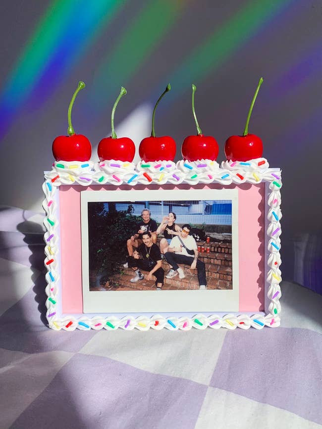 A frame with frosting and sprinkle outline and five 3d cherries on top