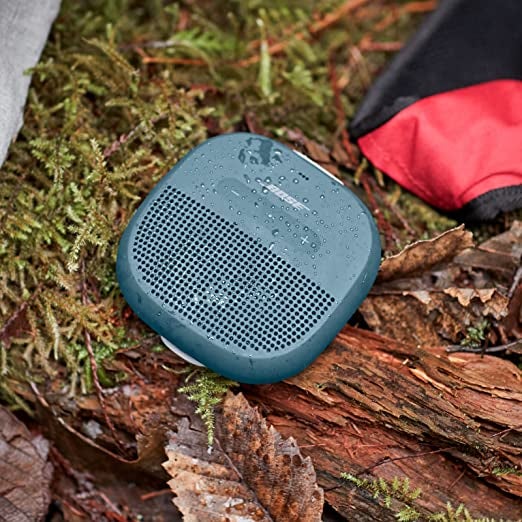 a wet blue bluetooth speaker sitting on a log outside