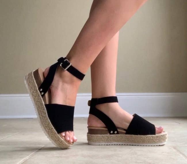 reviewer wearing sandals with tan braided flatform and black straps and toe bands