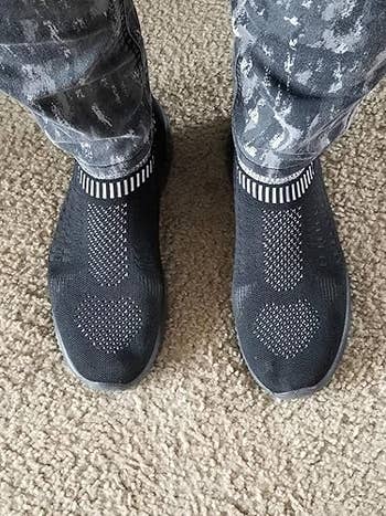 Person wearing patterned pants and knitted slip-on sneakers, showcasing a stylish and casual manner choice