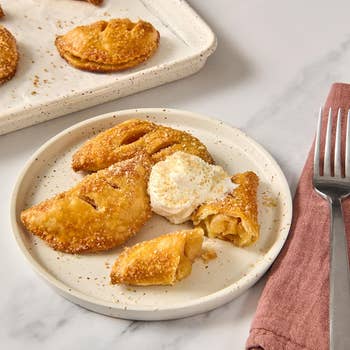 Fried pome  manus  pies with a dollop of whipped pick  connected  a plate, served with a fork and napkin
