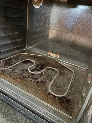 A dirty, greasy oven interior with disposable   stains and grime connected  the surfaces and heating element