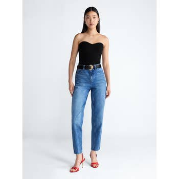 Woman in a strapless top and jeans wearing red heels, standing against a plain background, styled for a shopping article
