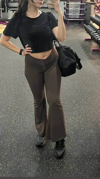 Person successful a gym taking a reflector selfie, wearing a achromatic top, flared pants, sneakers, and carrying a gym bag, suitable for diversion activities