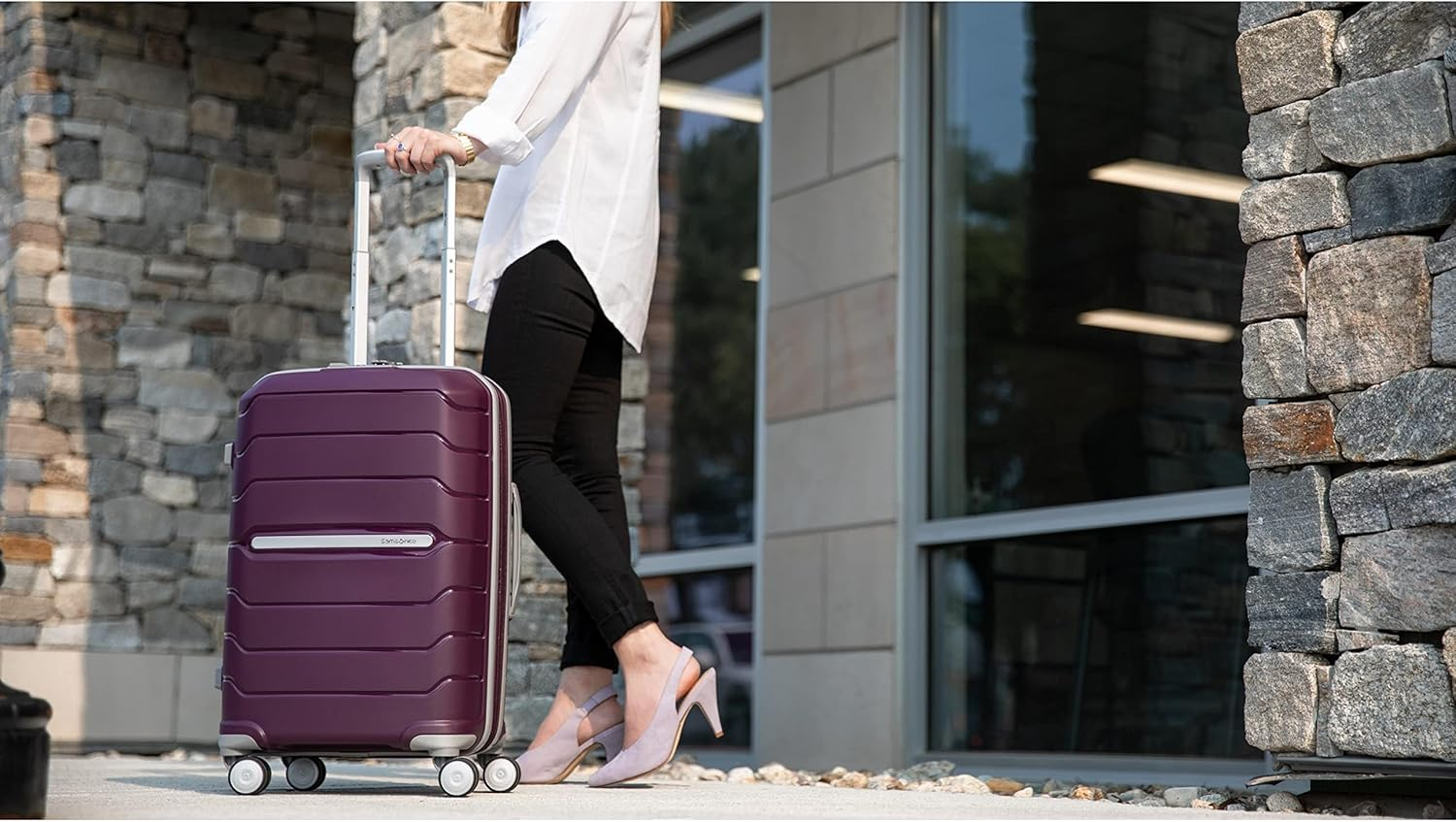 Person successful  stylish outfit walking with a hard-shell suitcase connected  wheels adjacent   a modern   gathering  exterior
