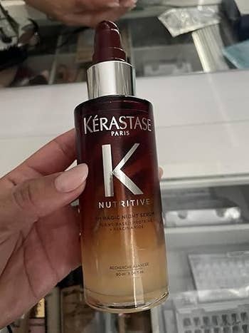 Hand holding vessel of Kérastase Paris Nutritive 8H Magic Night Serum, connected show successful a retail setting