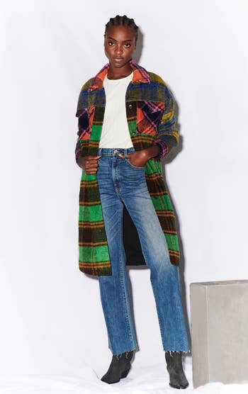 front of a model wearing a multicolored plaid long jacket over a white tee and blue jeans