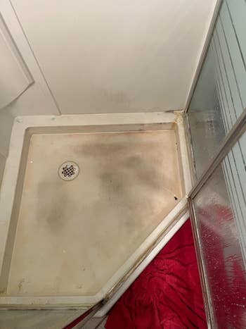 A dirty shower base with a red towel on the side, in need of cleaning products