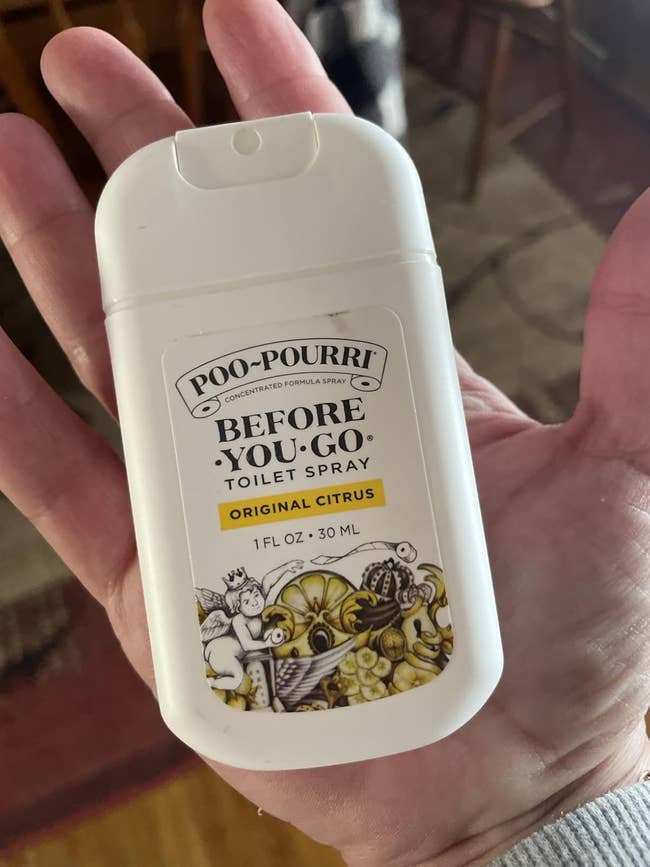 Person holding a tiny vessel of Poo-Pourri Original Citrus toilet spray
