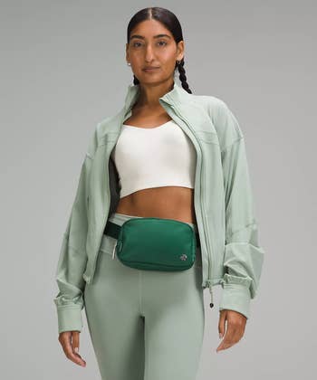 Person in a stylish, casual athleisure outfit with a zip-up jacket, crop top, leggings, and a waist bag, posing confidently for a shopping article