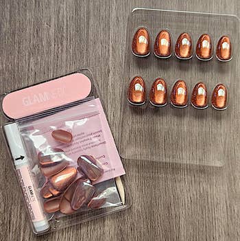 False nails acceptable   featuring glossy, metallic copper and pinkish  accents connected  a woody  surface, adjacent  to pinkish  packaging and adhesive