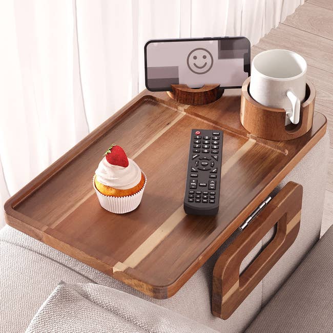 Wooden armrest tray array with a telephone holder, distant control, cup, and cupcake connected a sofa arm, perfect for convenient surviving country use