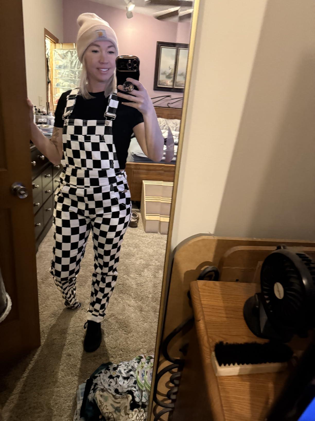Person successful  checkered overalls, achromatic  tee, and beanie, taking a reflector  selfie successful  a casual chamber  setting