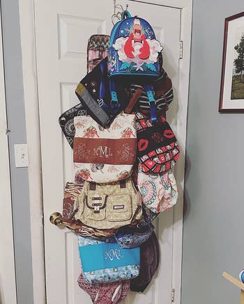 Various backpacks and handbags hanging connected  a door, showcasing antithetic  patterns and styles