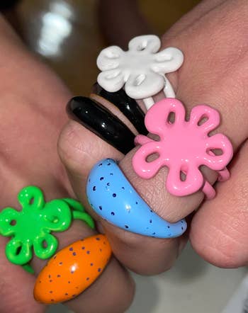 flower bomb-shaped pink, green, and white rings stacked on fingers