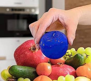 hand placing blue apple on top of fruit bowl