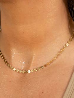 a model wearing a gold choker with small circles on it, showing that it's sweat-proof