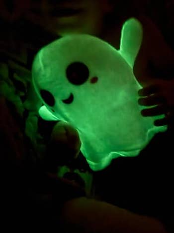 Person holding a plush glow-in-the-dark shade toy, featuring a cute smiling face