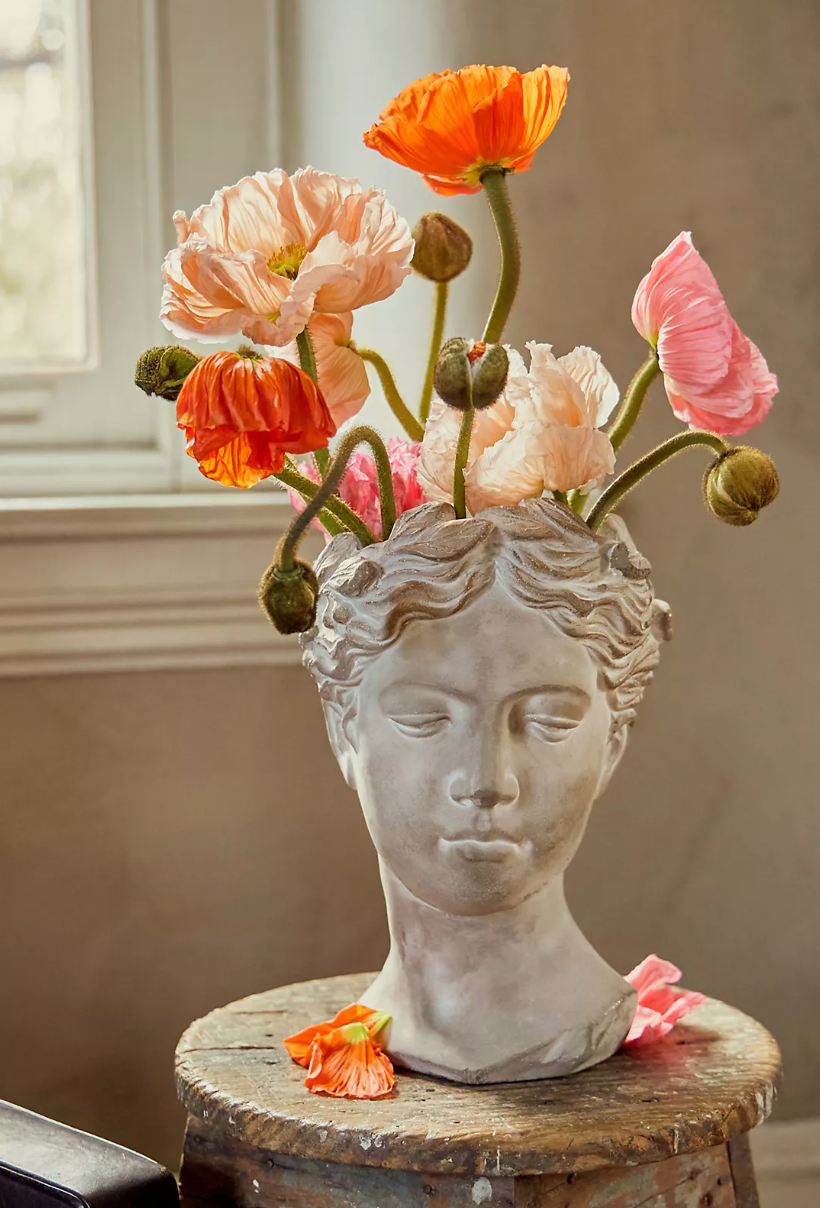 A white faded Grecian-inspired bust serving as a vase for colorful flowers that emerge from the haed 