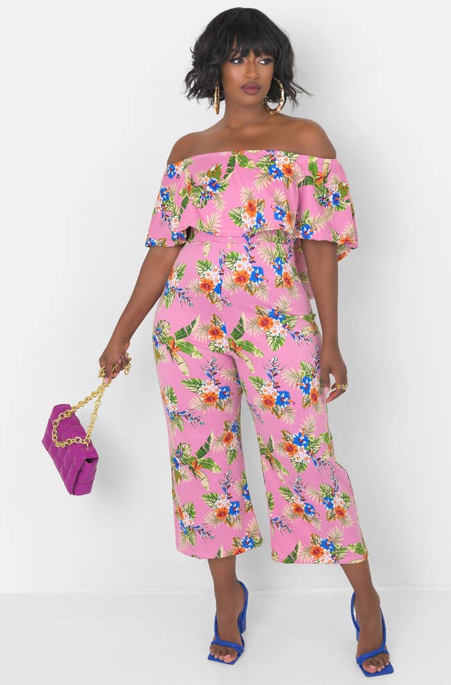 model in pink jumpsuit with off the shoulder ruffle top and blue white and orange tropical floral print