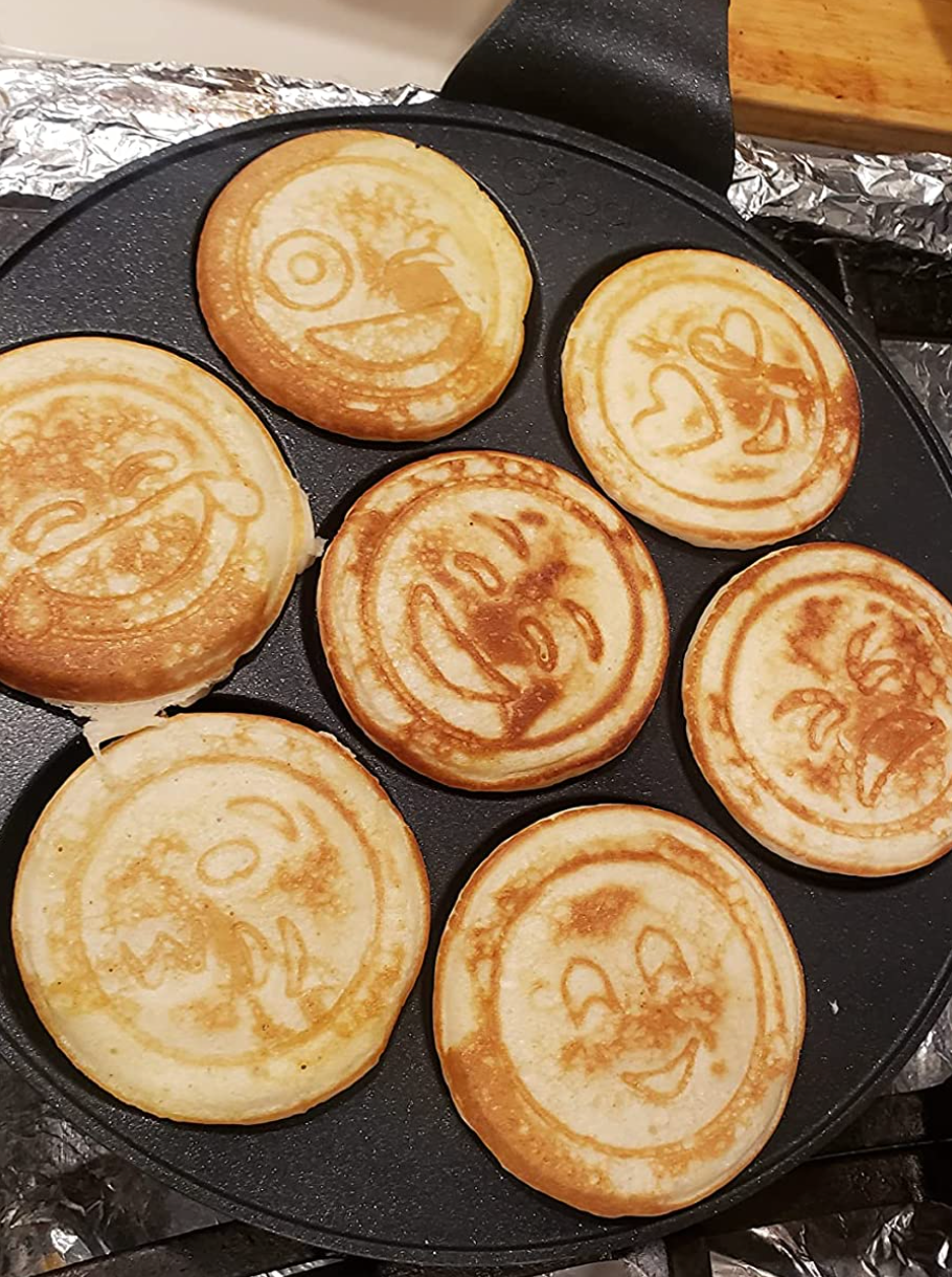 A pan with mini pancakes that all have different expressions cooked into them 
