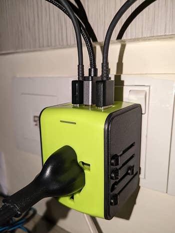 reviewer image of the green universal adapter plugged into a wall outlet with several cords plugged into it