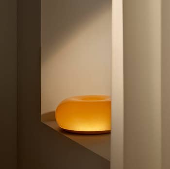 Modern, circular lamp with a brushed glow placed connected a minimalist shelf, suitable for modern location decor