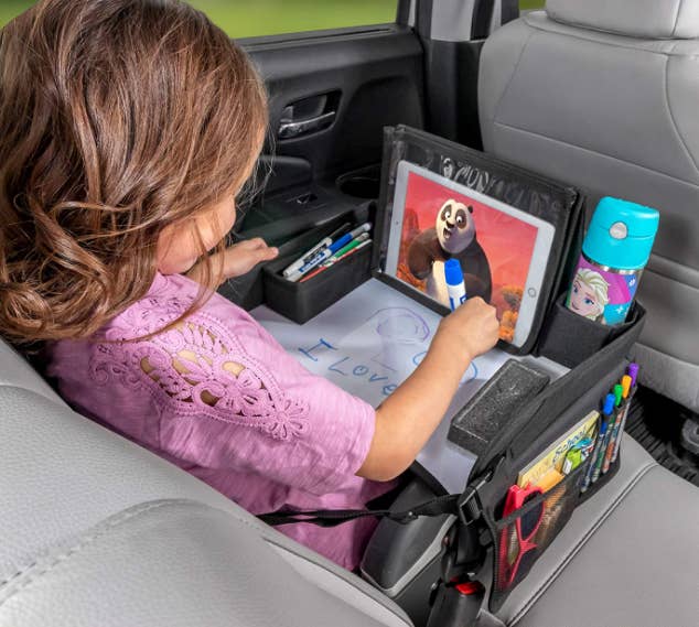 toddler in car seat with the tray placed over them while they draw and watch movie on tablet
