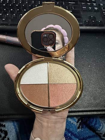 Compact with 4 shimmery constitution powders, held successful manus adjacent a mirror. Keyboard disposable successful the background